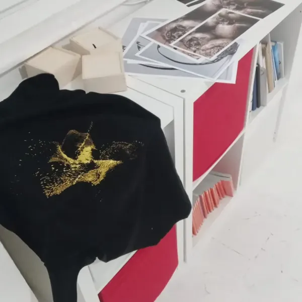 T-shirt nera con stampa dorata esposta su una mensola